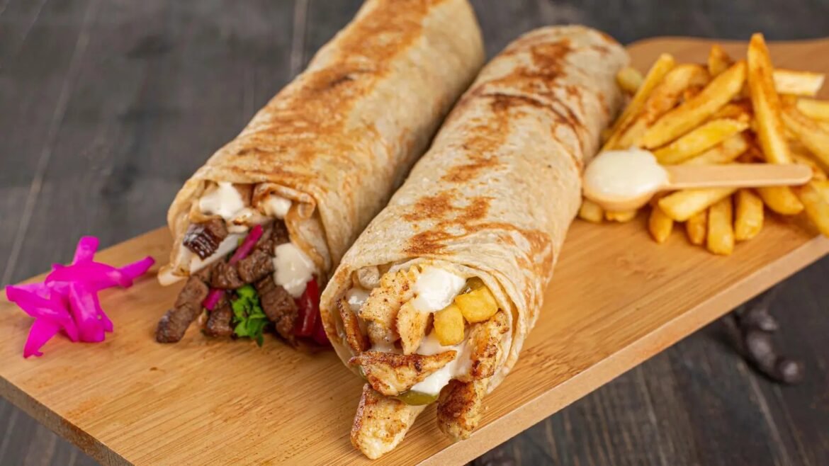 Two grilled wraps filled with meat, vegetables and melted cheese, served on a wooden board with french fries on the side.