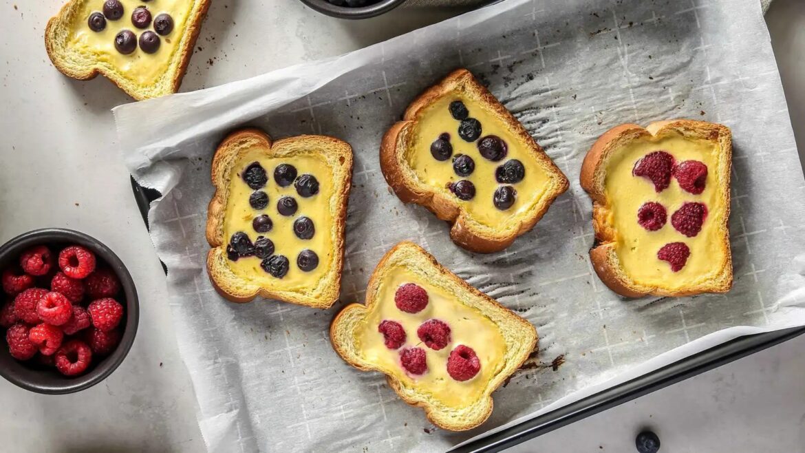 Toasts with yellow custard and berry toppings on parchment, featuring blueberries and raspberries.