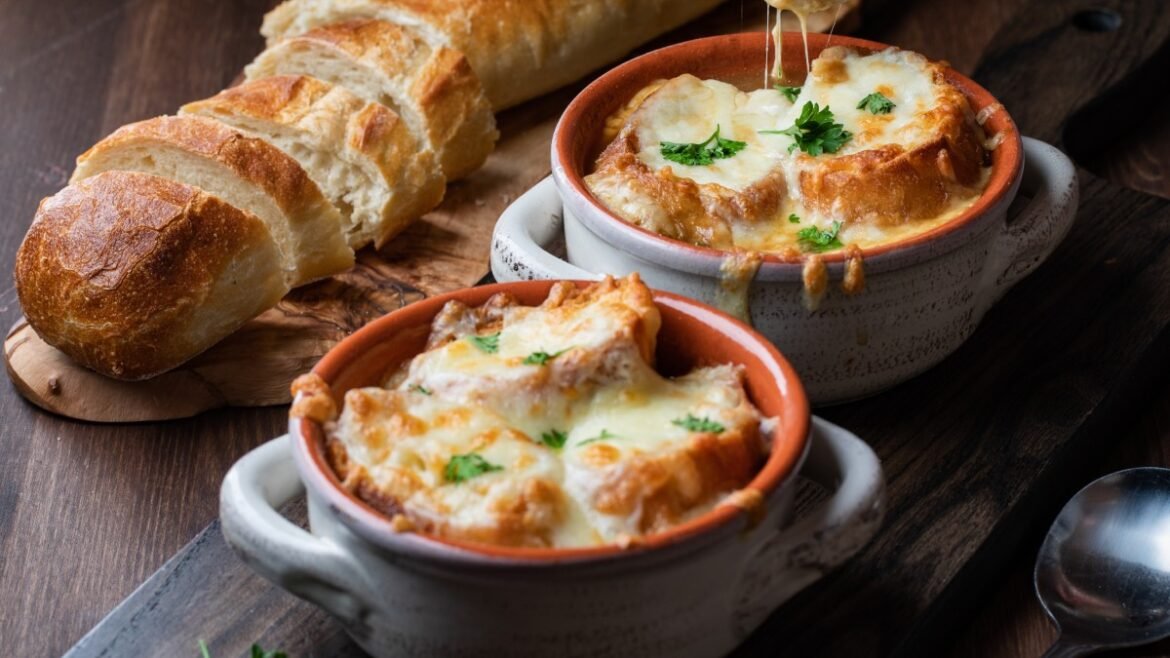 Two baked cheese gratin dishes with melted cheese and parsley on a dark wooden table, with a sliced baguette nearby.