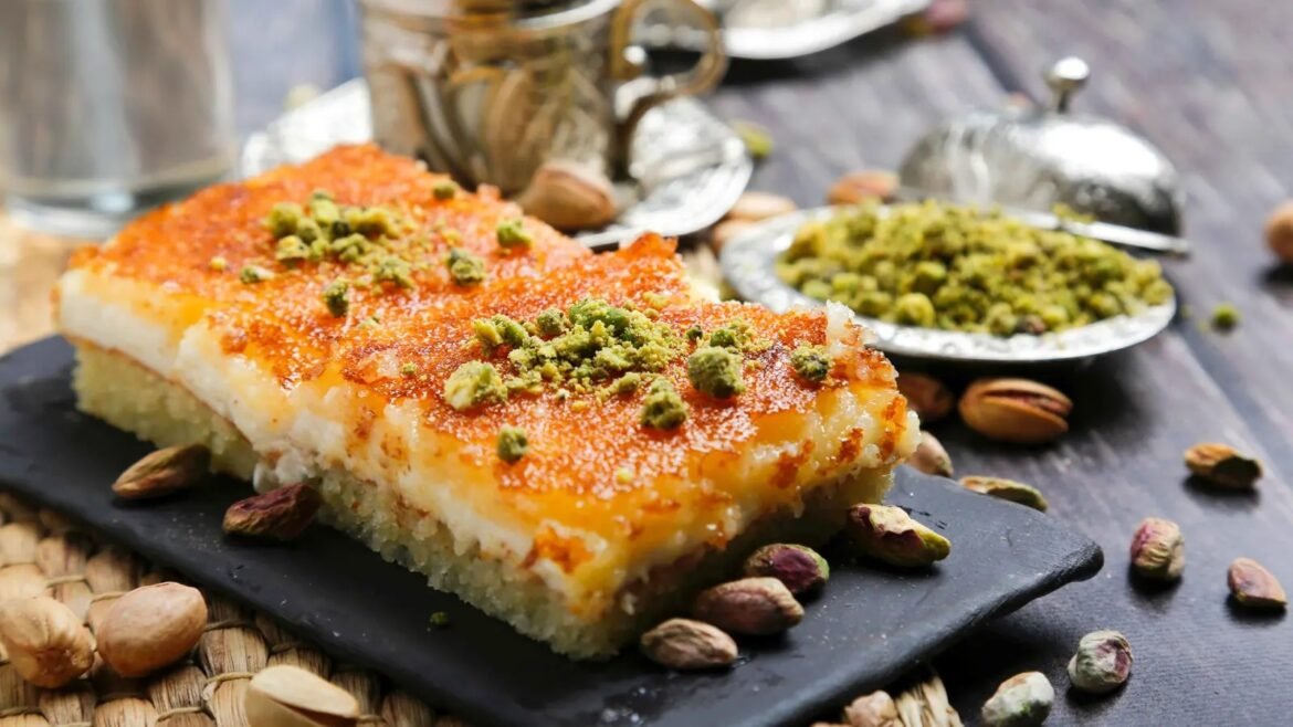 Two pistachio-topped citrus dessert bars on a black slate with scattered pistachios around them.