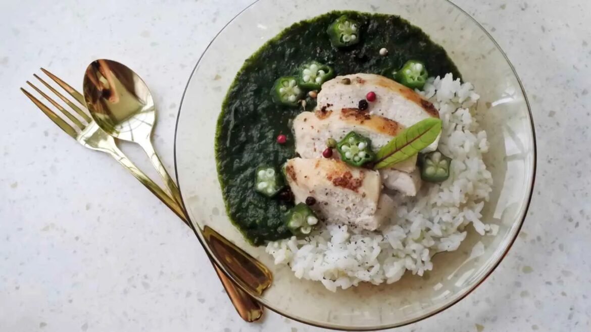 Plate of sliced roasted chicken on white rice with green spinach sauce, okra spears, and peppercorn garnish topped with a bay leaf.