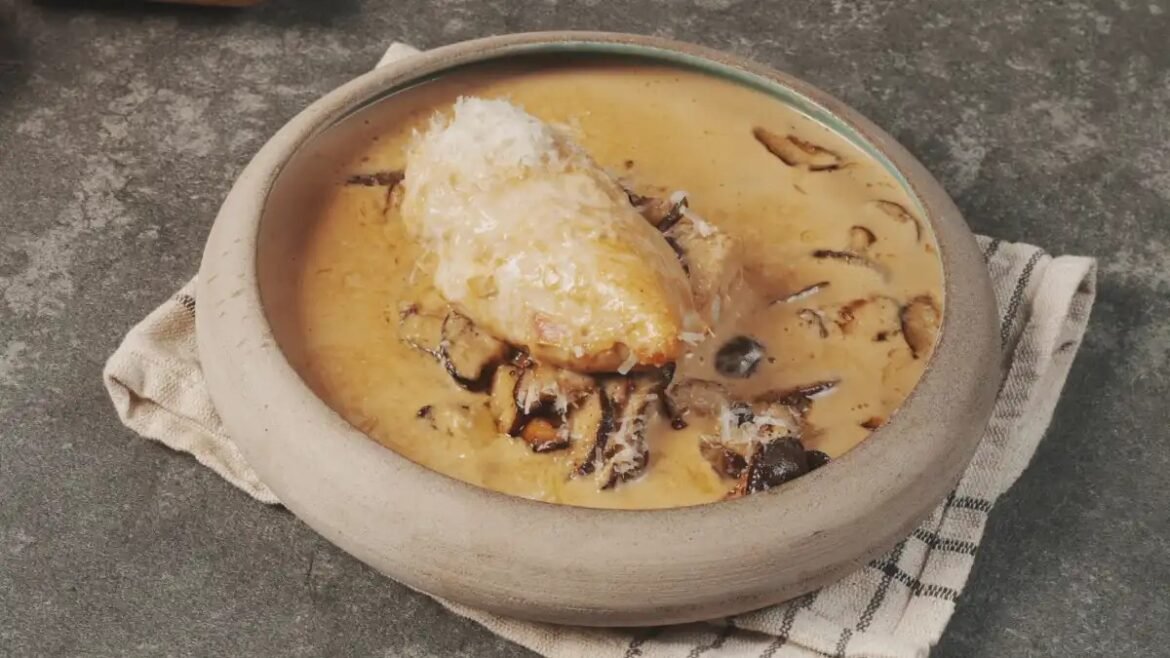 Creamy chicken and mushroom soup in a rustic stone bowl with a large chicken piece on top, placed on a striped towel.