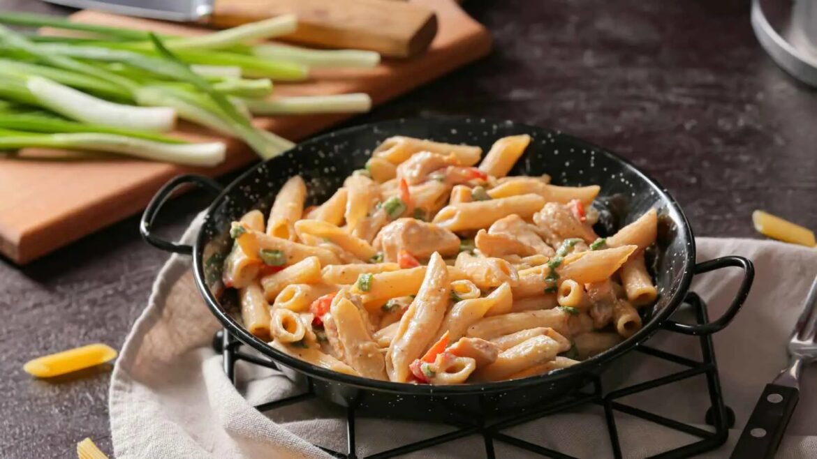 Penne pasta in a creamy chicken sauce with peppers in a black skillet on a kitchen counter