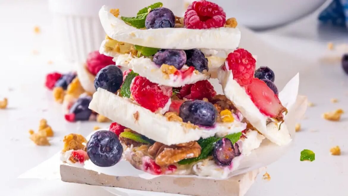 Stack of white crispy wafers layered with yogurt cream, blueberries, raspberries and strawberries, garnished with mint and granola crumbs.