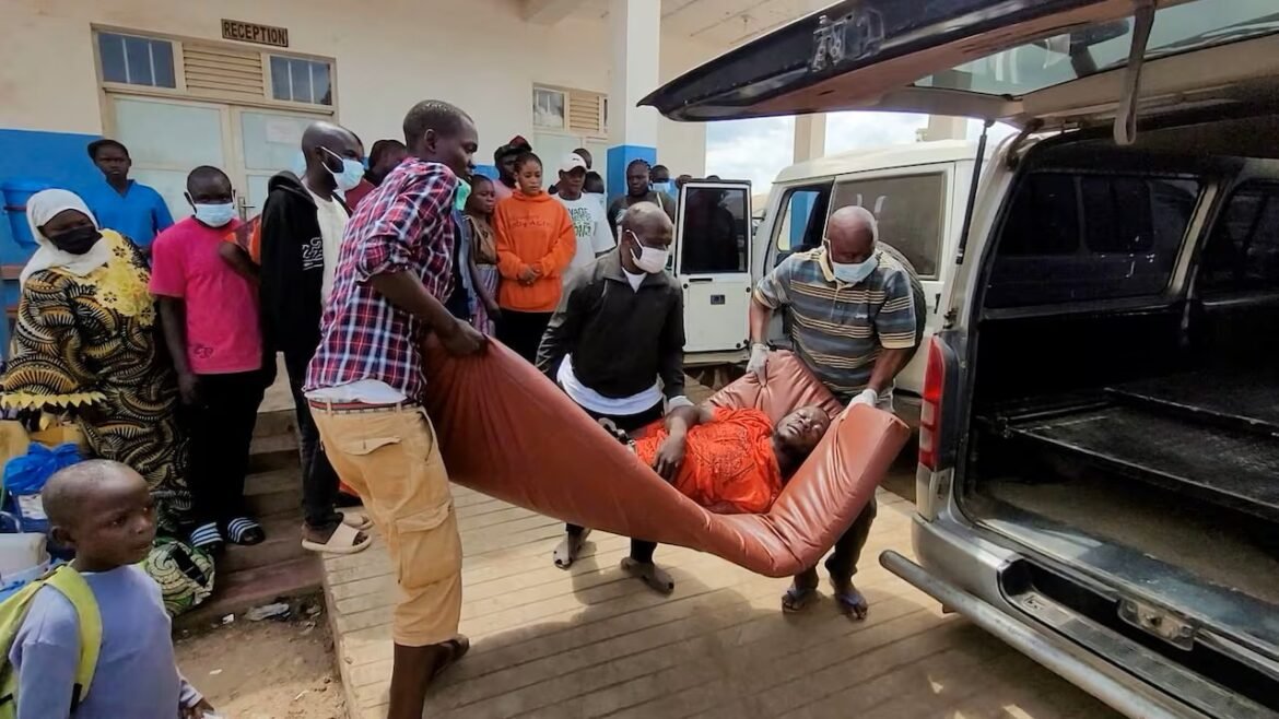 Group of people wearing masks assist a person on an orange stretcher being loaded into a white van with open rear doors outside a building labeled Reception.