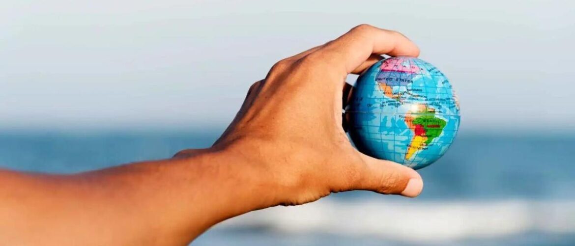Hand holding a small globe near the sea, symbolizing travel or global reach.