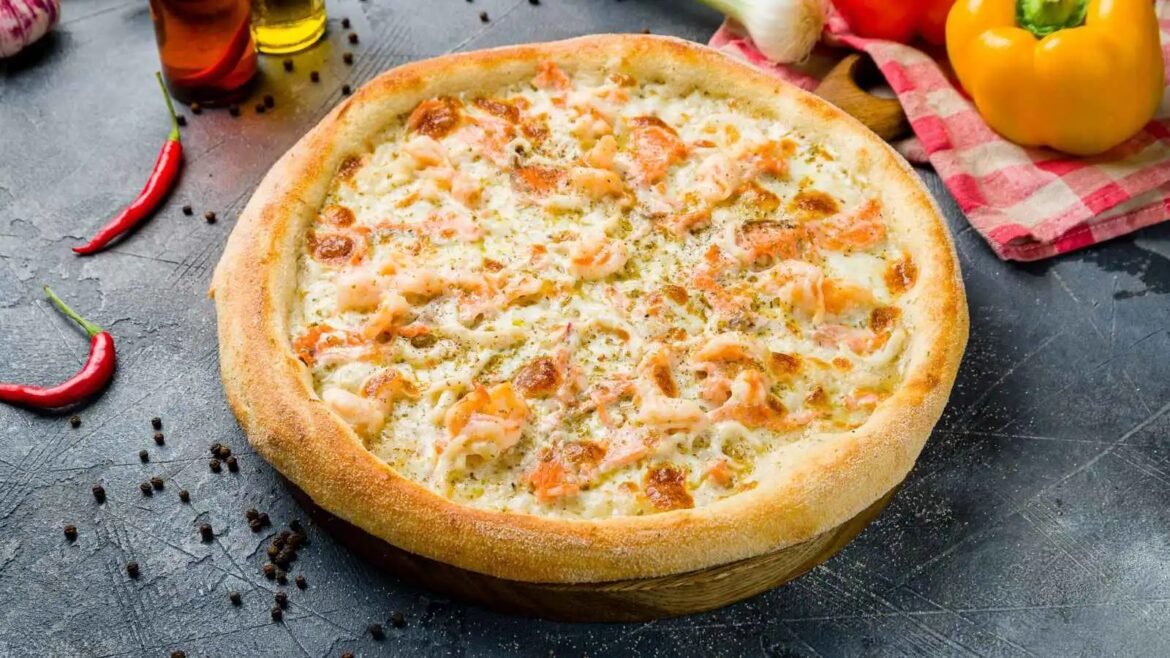 Round pizza with shrimp and melted cheese on a golden crust, framed by peppers and spices on a dark surface, rustic scene.