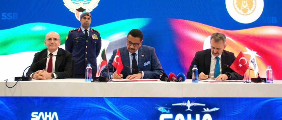 Three men sign documents at a formal signing ceremony, with a uniformed guard standing behind and Turkish flags on the desk against a blue backdrop.