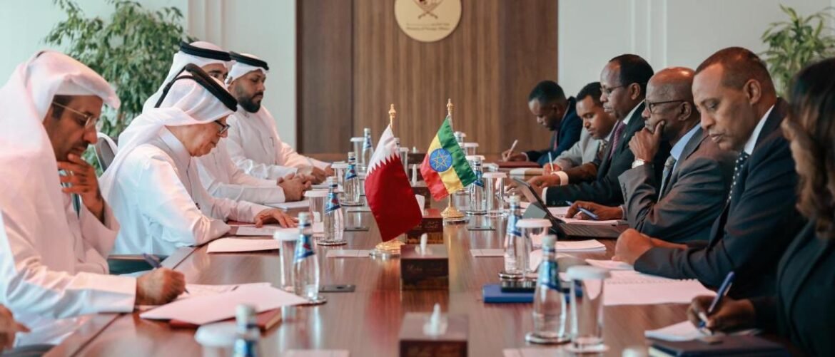 Diplomatic meeting around a long conference table with officials in traditional robes and suits, flags at the center, signing documents.