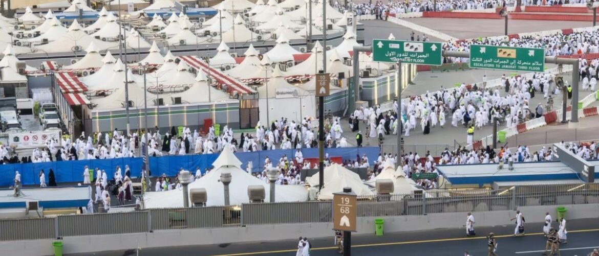 Large tent city for Hajj pilgrims with white ihram robes and crowded walkways.