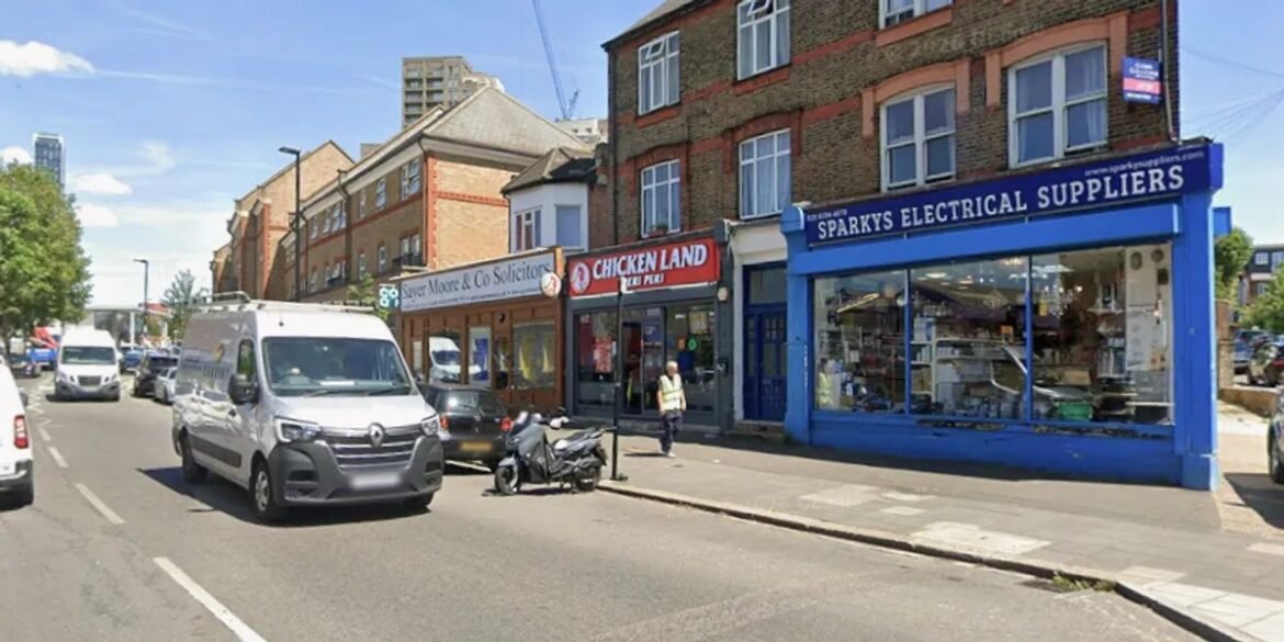 Street view with shops including Sparks Electrical Suppliers in a blue storefront and Chicken Land beside a solicitor's office on a sunny day.