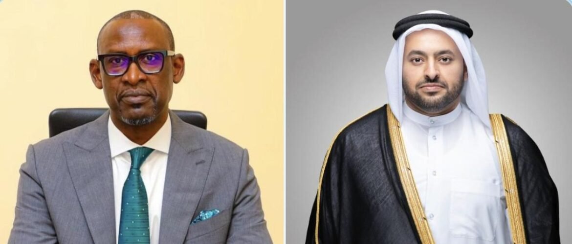 Two men shown side by side: left in a gray suit with teal tie and glasses, right in white thobe with a black-and-gold bisht.