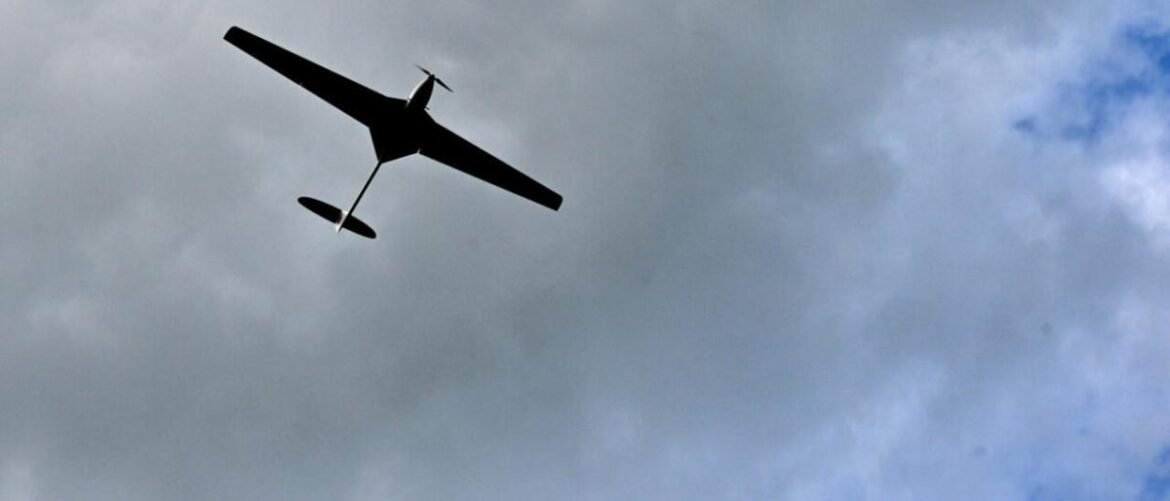 Silhouette of a small single-engine glider aircraft flying against a cloudy sky.