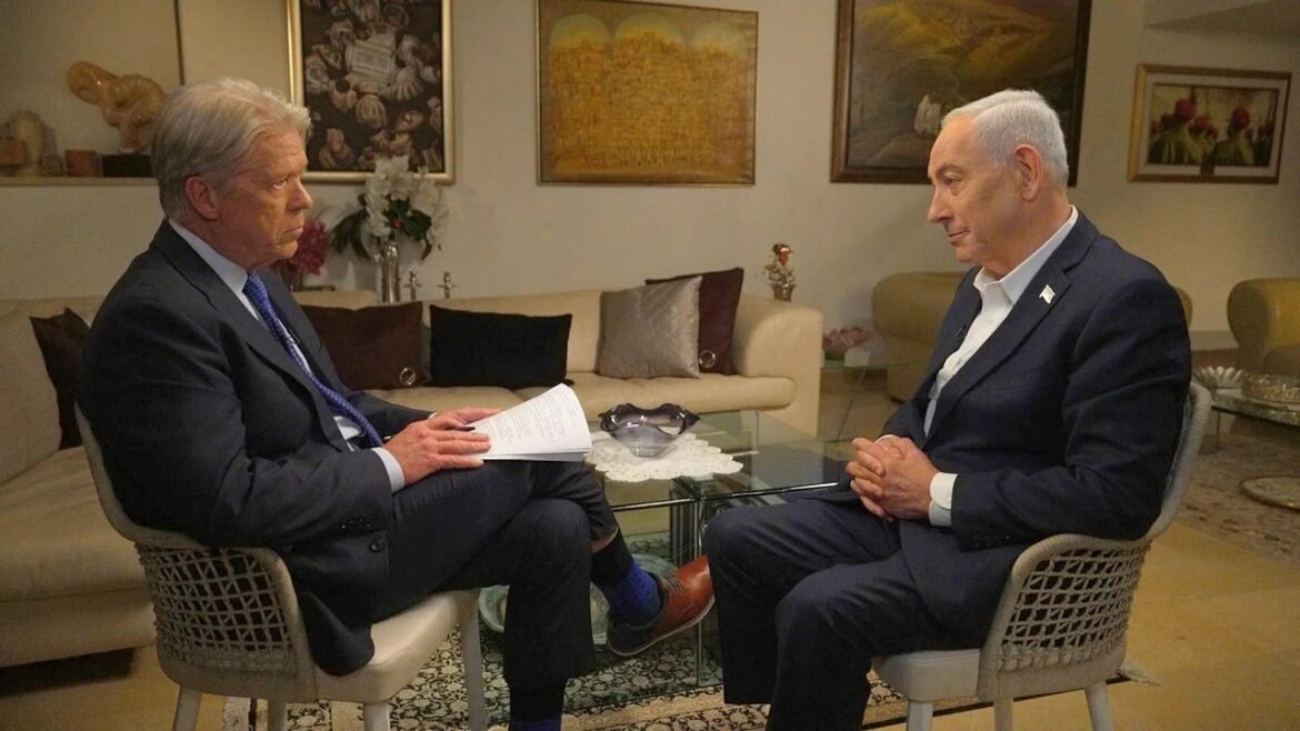 Two men in suits sit across from each other in a living room, one holding papers, as they discuss a formal matter.