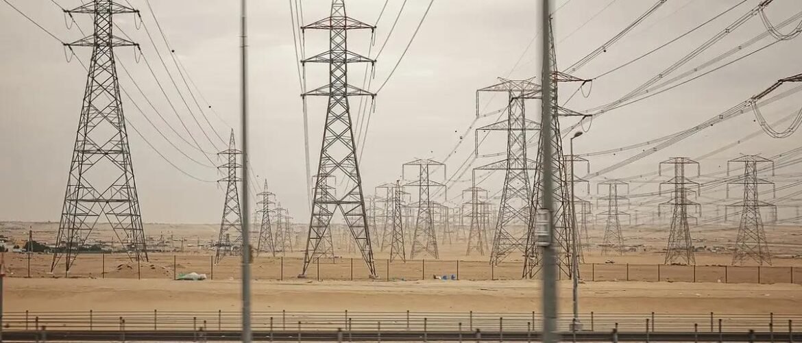 Desert scene with numerous lattice electricity pylons and overhead power lines receding into the distance.