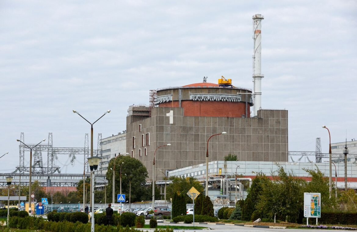Industrial power plant with a large orange-domed circular roof and tall smokestack, surrounded by a parking lot and street lamps in the foreground to give scale.