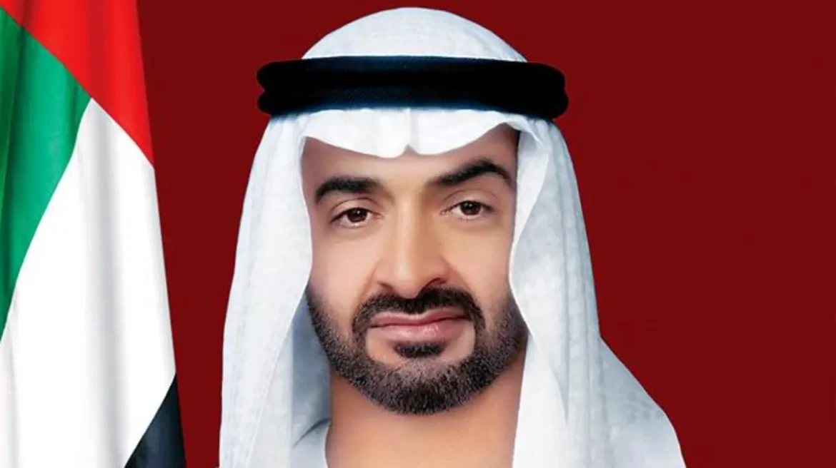 Portrait of a man in traditional UAE attire (white ghutra and kandura) with a UAE flag in the background on a red backdrop.