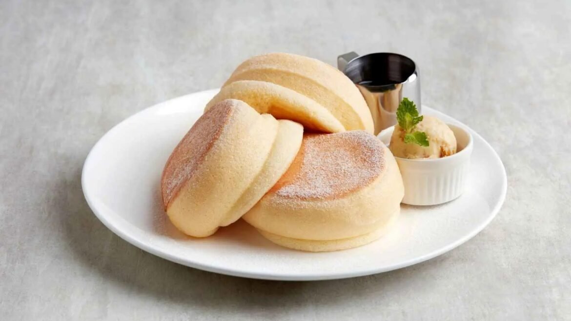 Stack of fluffy, sugar-dusted round cakes on a white plate with a side scoop of ice cream and mint garnish.