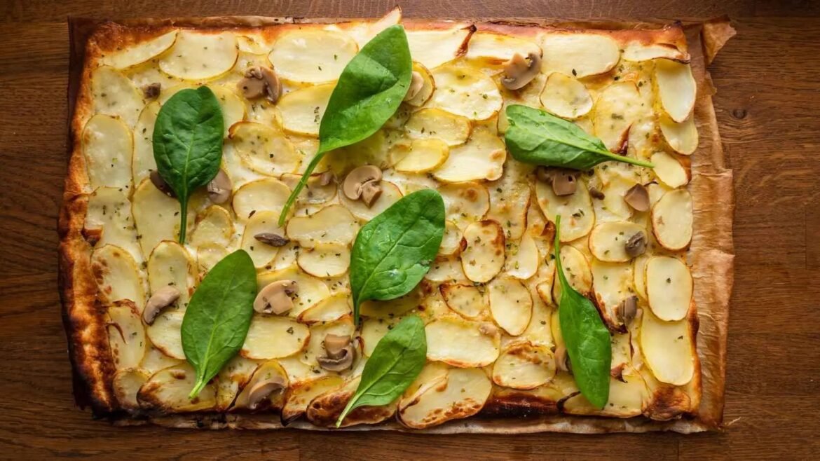 Potato-topped flatbread pizza with mushrooms, melted cheese, and fresh spinach on a parchment-lined baking sheet.