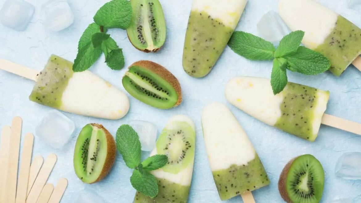 Kiwi popsicles on sticks with mint leaves and kiwi slices on a light blue surface.