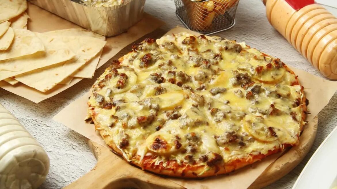 Pizza topped with pineapple and mushrooms, melted cheese, on a wooden board with chips and a pasta roller nearby for context.
