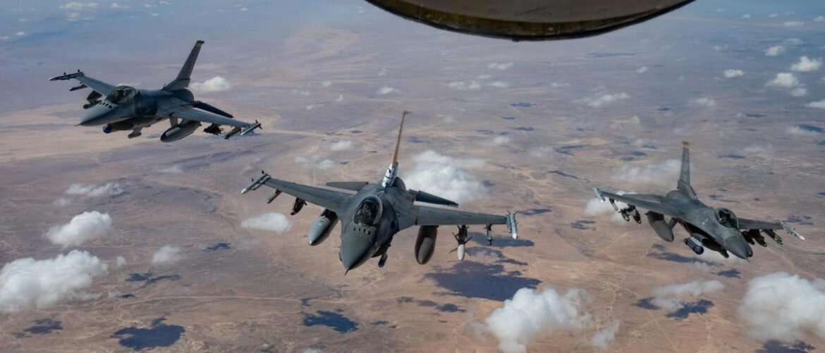 Three fighter jets flying in formation over a desert landscape with scattered clouds above them.