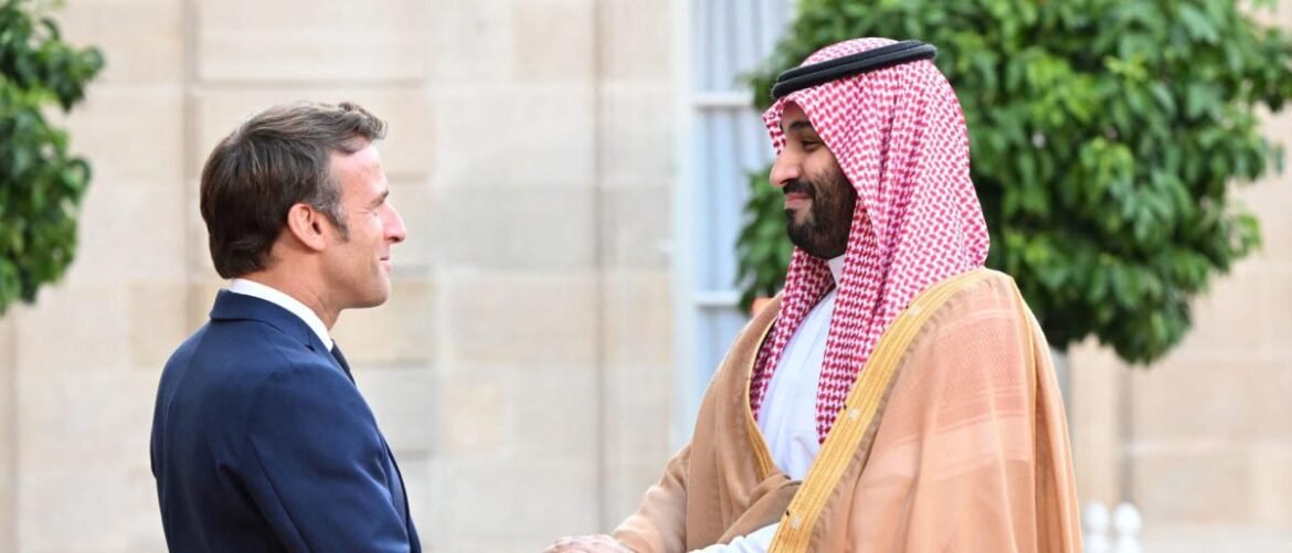 Two men greet with a handshake: a businessman in a navy suit and a man in a traditional beige thawb with a red-and-white keffiyeh.