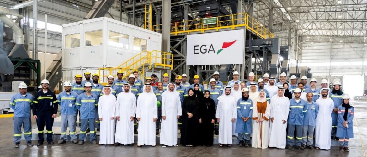 Group of factory workers and executives posing for a team photo in an industrial plant with an EGA banner in the background.