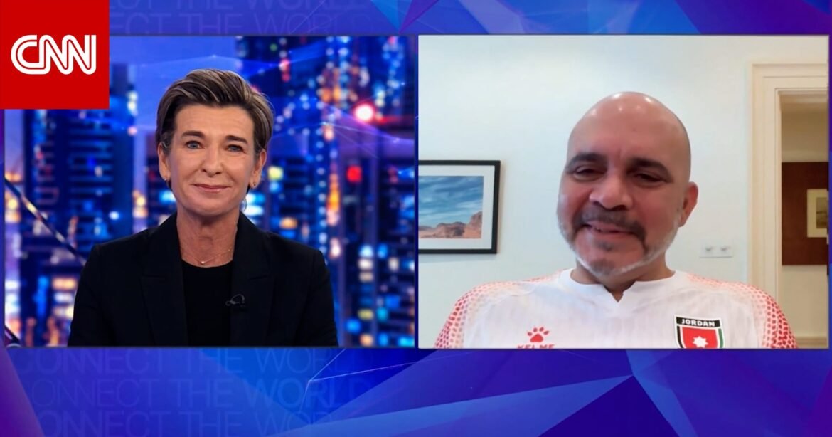 Split-screen CNN interview: female anchor in studio left, city-lit background; guest in a white and red sports jersey on the right via video call.
