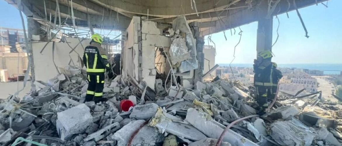 Firefighters in full protective gear standing amid rubble of a collapsed building, inspecting debris with a coastal city in the background.