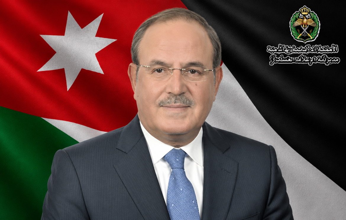Portrait of a middle-aged man in a dark suit and blue tie, posed in front of the Jordanian flag with a government emblem in the corner.