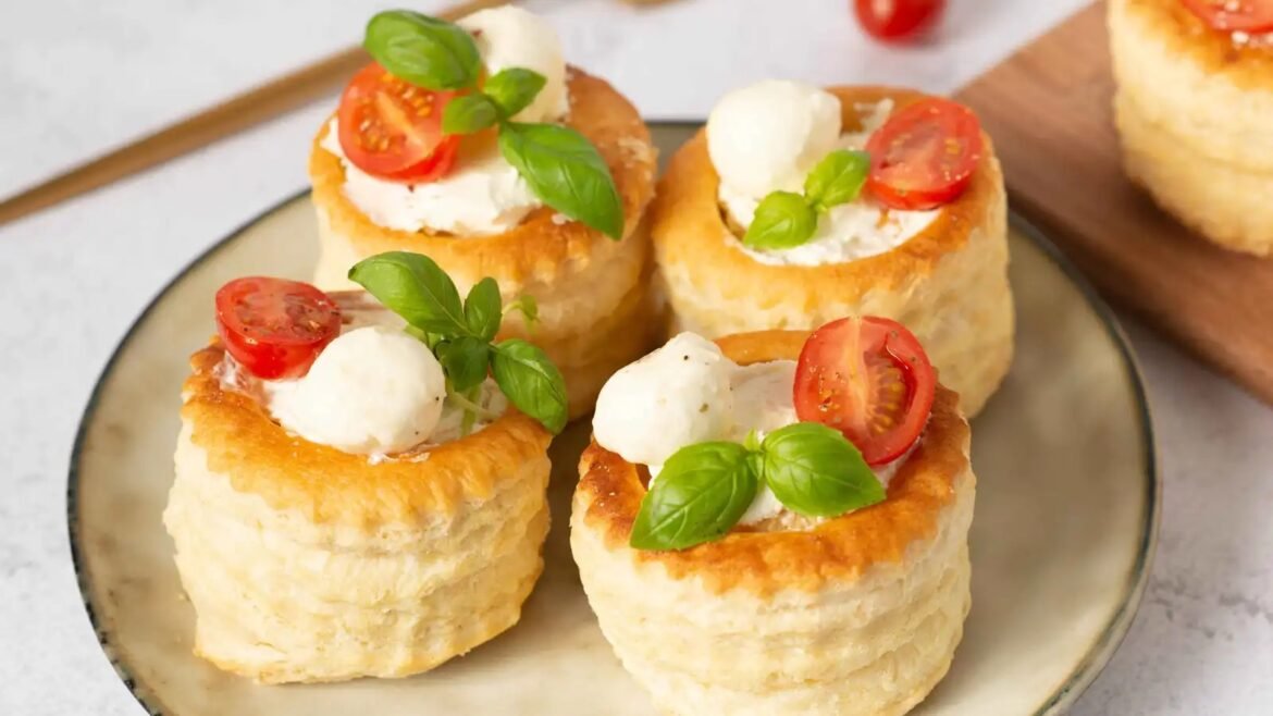 Mini savory puff pastry bites topped with cream cheese, cherry tomatoes, mozzarella balls, and basil on a plate