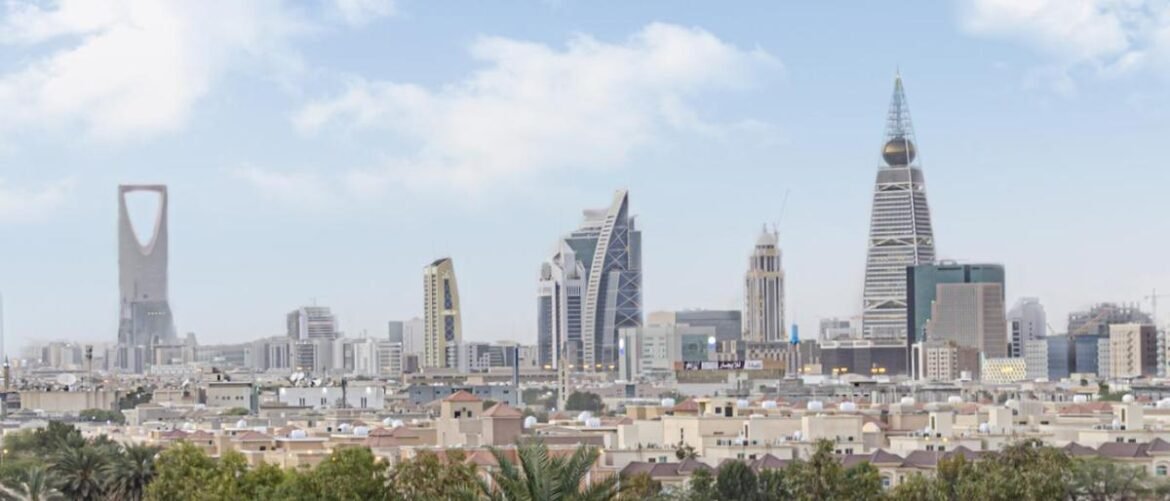 City skyline with distinctive skyscrapers rising above a low-rise foreground under a blue sky, including a tall arch-shaped tower and other modern towers