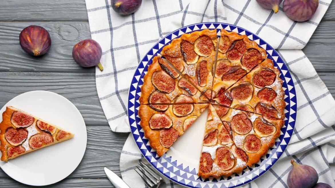 Fig tart topped with sliced figs on a blue patterned plate, with a single slice served on a white plate nearby and fresh figs around.