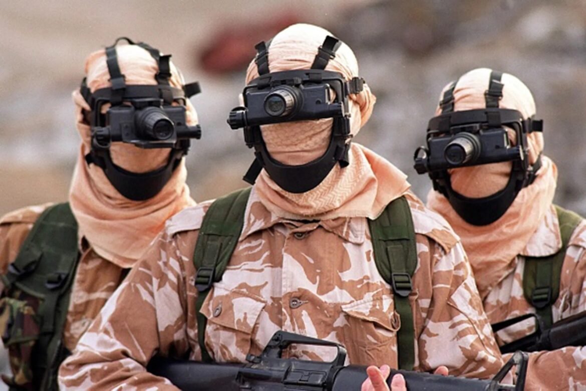 Three soldiers in desert camouflage with night-vision goggles mounted on their helmets, holding rifles in a ready position.