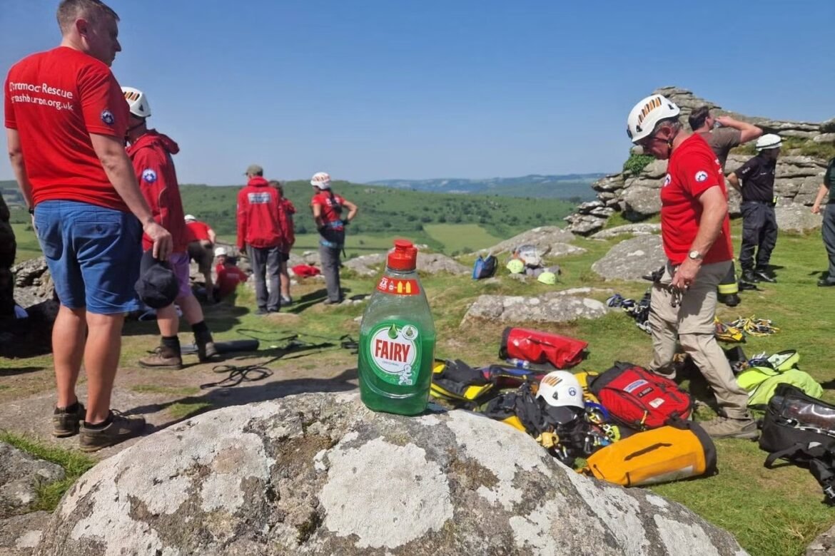 Group of mountain rescue volunteers in red shirts gather on a rocky hill, gear laid out nearby, with a Fairy bottle in the foreground on a rock.