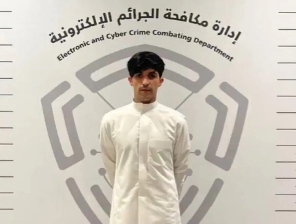 Man in a white traditional robe standing with hands behind his back in front of a wall displaying the Electronic and Cyber Crime Combating Department logo and text.