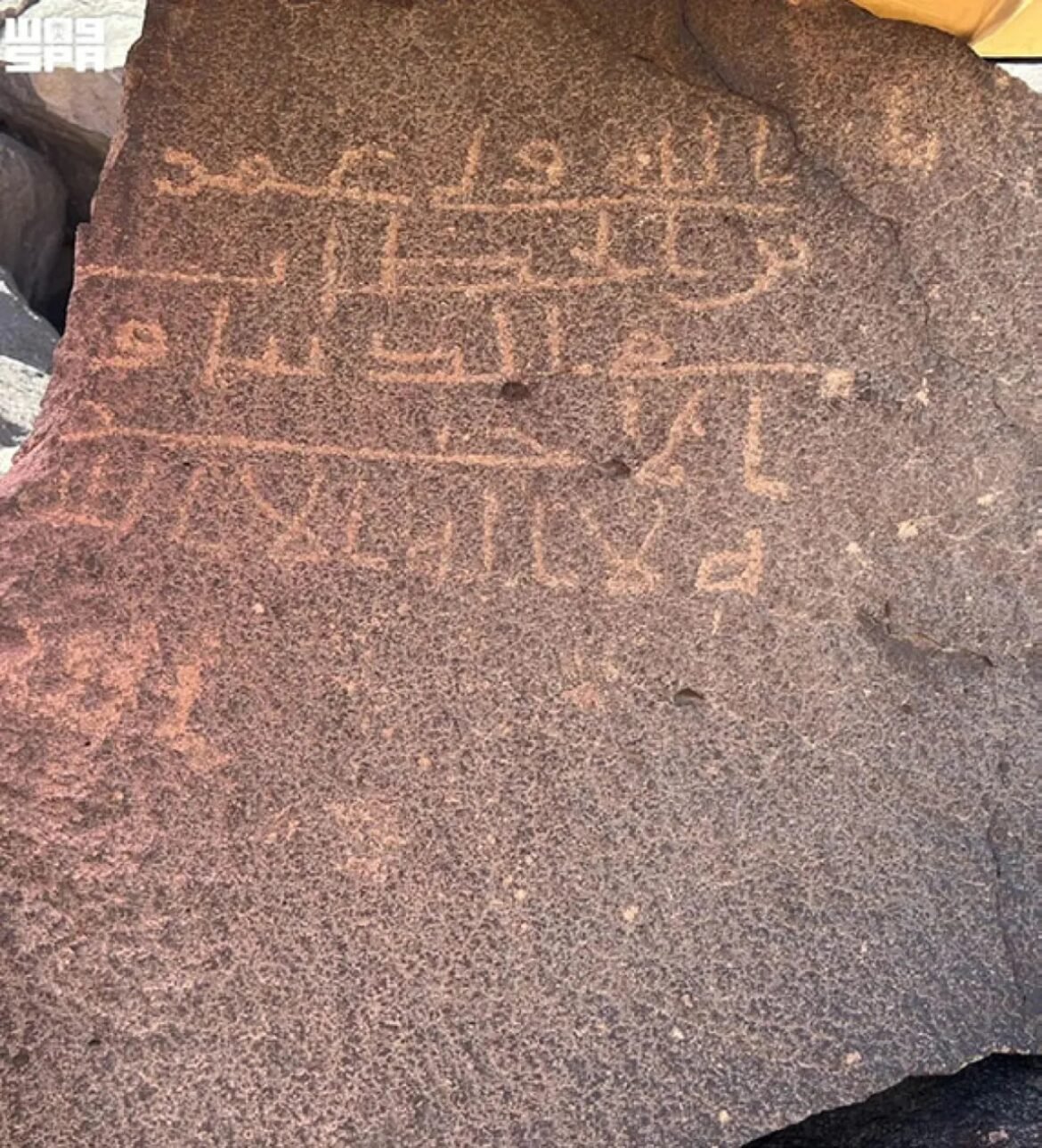 Rock surface with shallow orange-brown petroglyphs/inscriptions in geometric shapes across the stone surface.