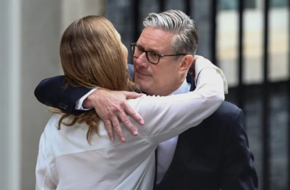 Two professionals hug warmly outdoors; man with gray hair and glasses in a dark suit.