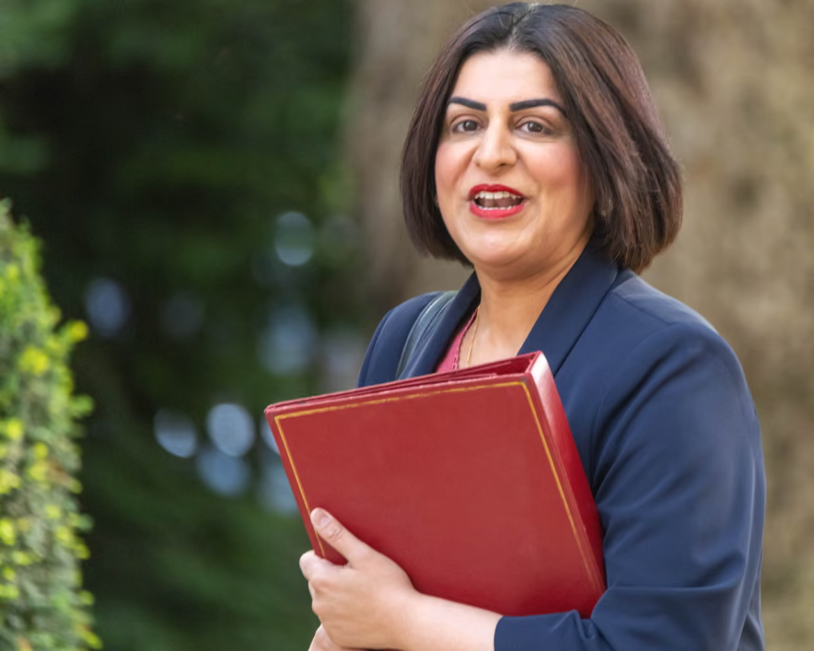 Professional woman in a navy blazer holding a red binder outdoors, looking at the camera and smiling.
