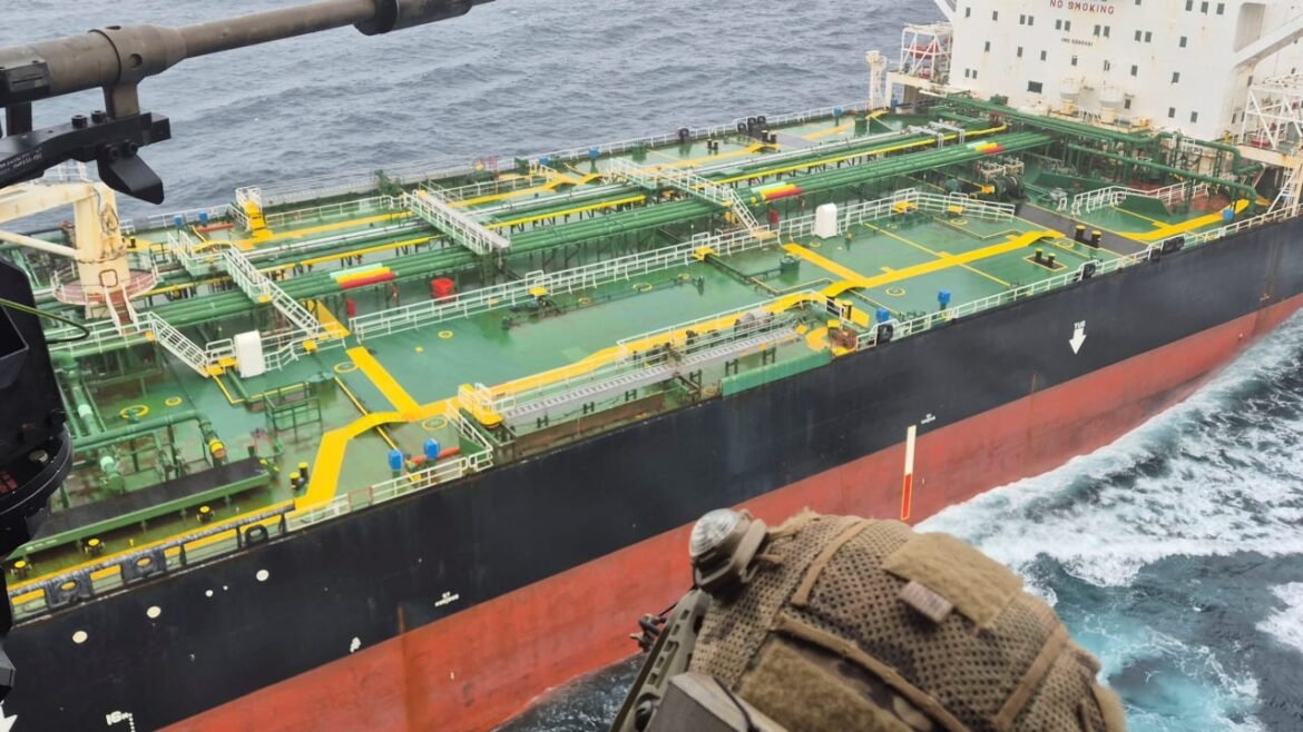 Aerial view of a large vessel at sea with a green deck, yellow walkways, and extensive piping; foreground shows a person wearing a helmet far above the deck.