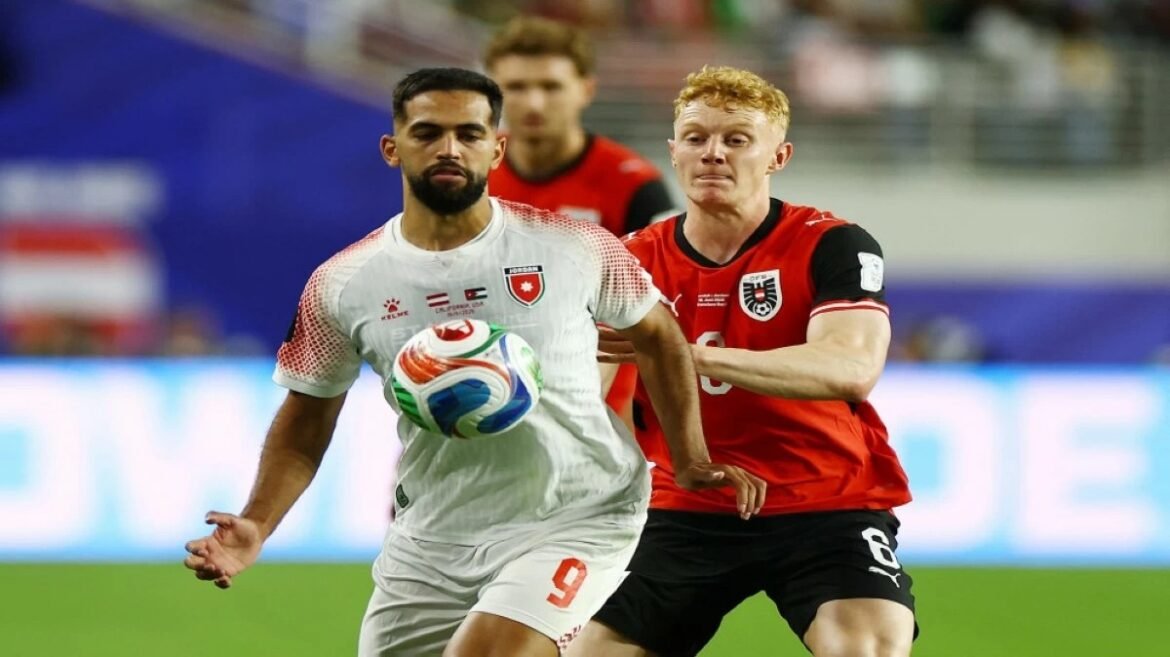 Soccer players chase a ball in a two-player tussle on the field, white jersey foreground and red jersey defender behind him