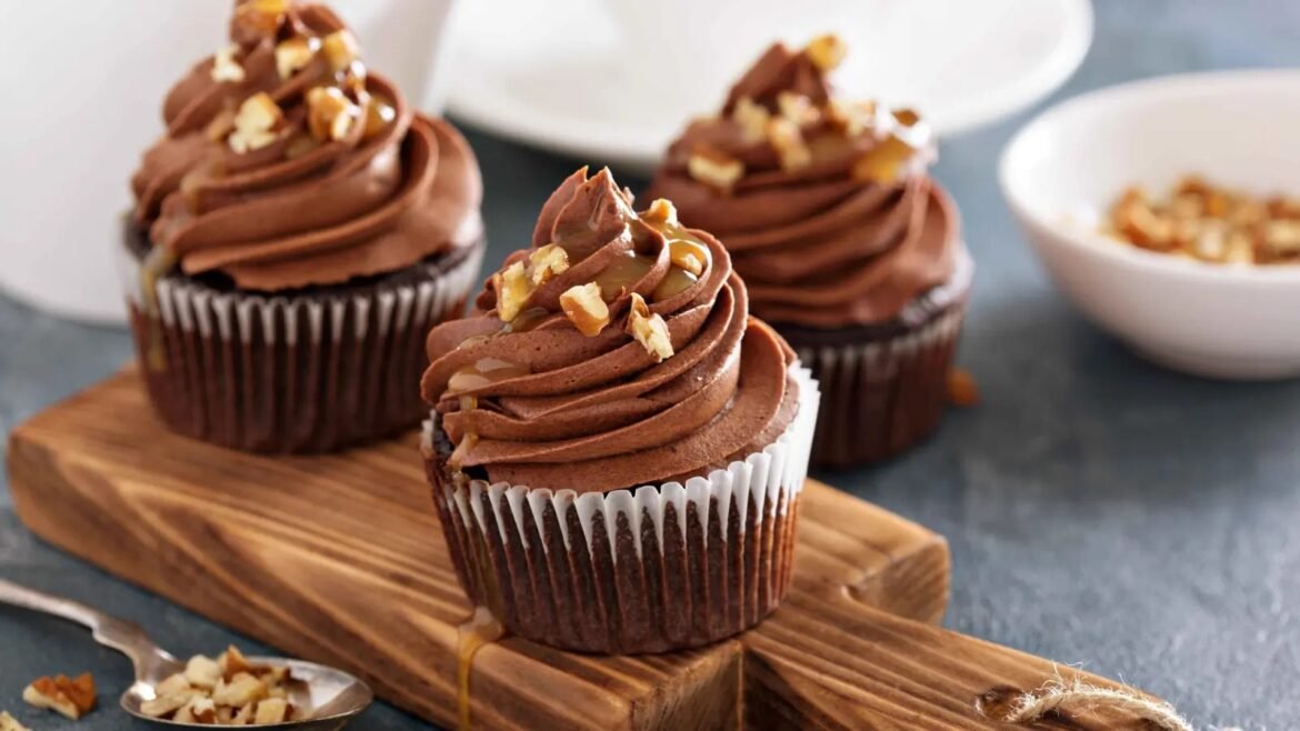 Chocolate cupcakes with swirled frosting and chopped nuts on a wooden board