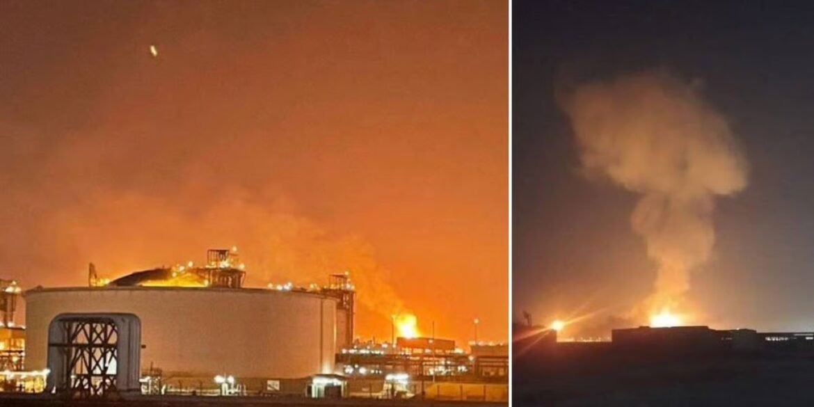 Nighttime industrial fire at a large chemical/oil facility with bright flames and smoke rising from storage tanks and processing units on the left and a distant blaze on the right.",