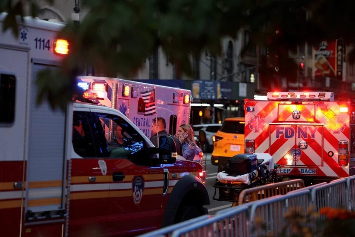 FDNY ambulance and responders on a city street at dusk, with a stretcher ready beside a barricade-lined sidewalk.