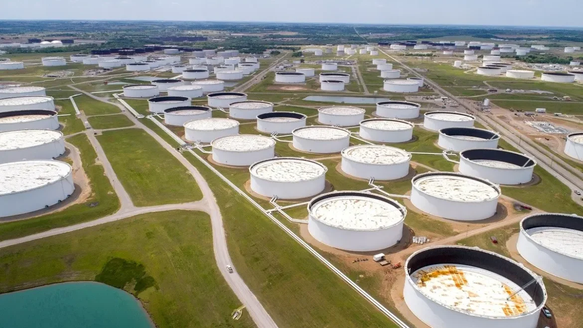 Aerial view of a vast oil storage tank farm with hundreds of white circular tanks and a network of roads.