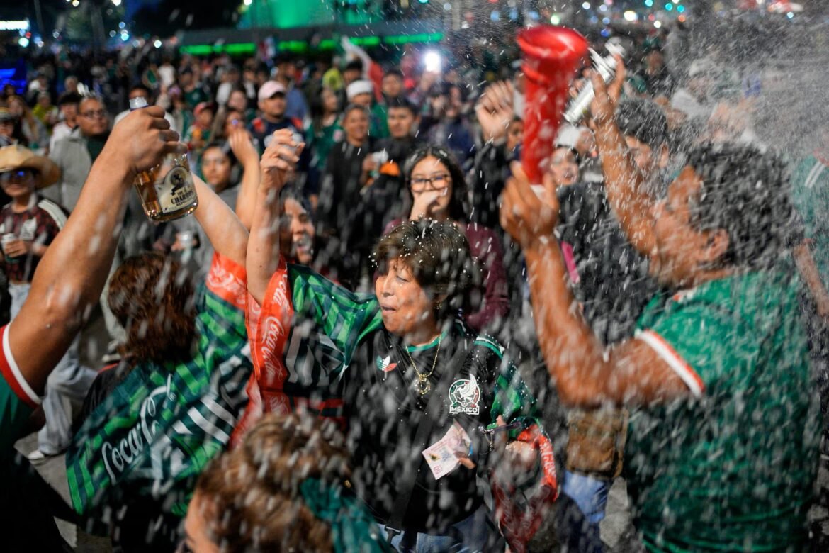 Crowd of sports fans celebrating with champagne spray, wearing green and black Mexico jerseys at a lively street party.