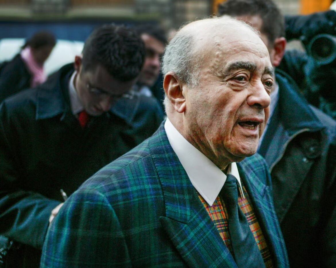 Older man in a green plaid blazer and tie speaking at a busy outdoor event in a crowd.