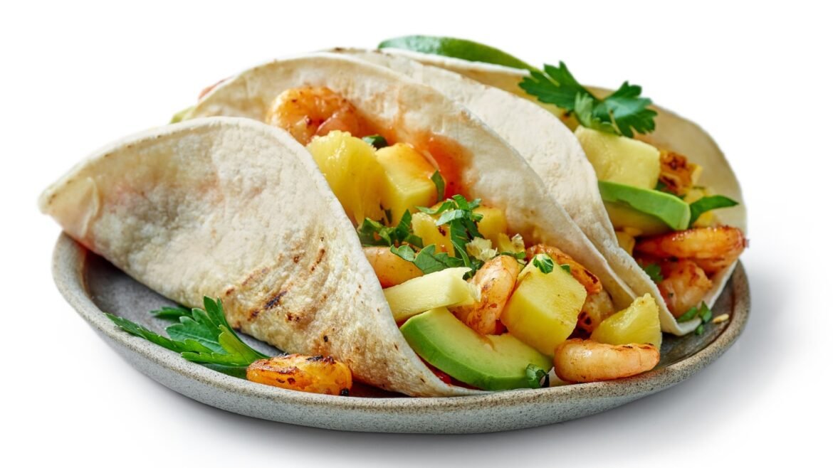 Three soft tacos filled with shrimp, pineapple and avocado on a gray plate, garnished with cilantro.