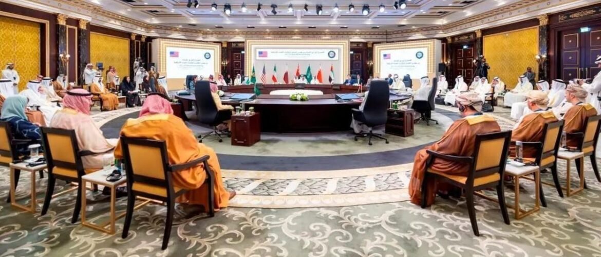 Delegates seated around a circular conference table in a grand meeting room with national flags and large presentation screens in the background.